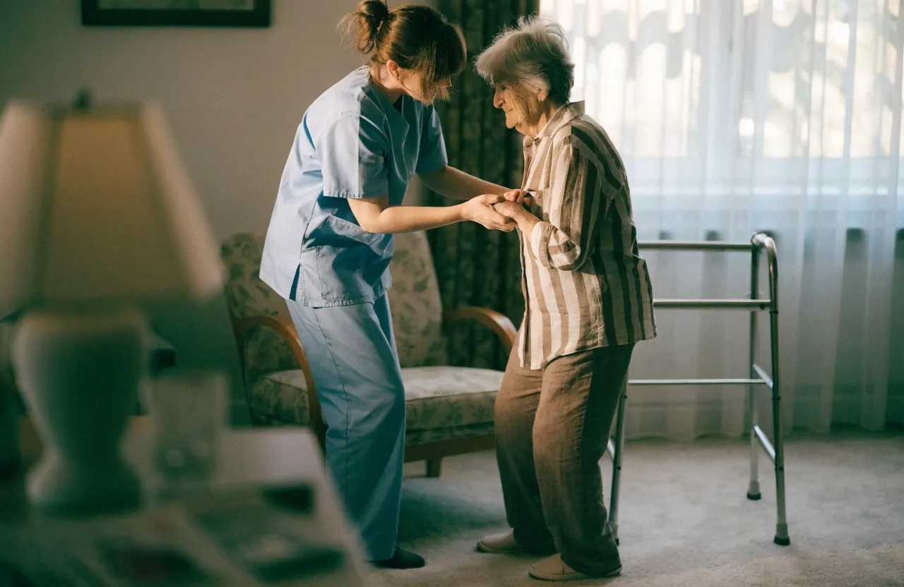 A personal support worker helping an older woman stand up in her living room.